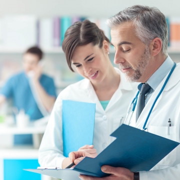 Confident doctor checking medical records on a clipboard with his female assistant, healthcare and professionalism concept